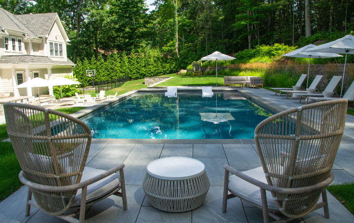 A picturesque pool scene with chairs and umbrellas in front of a house, enhanced by a comfortable lounge for leisure activities.