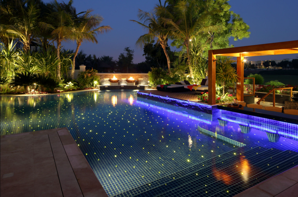 A beautifully lit pool showcasing underwater lights, accompanied by an inviting lounge area for relaxation and gatherings.