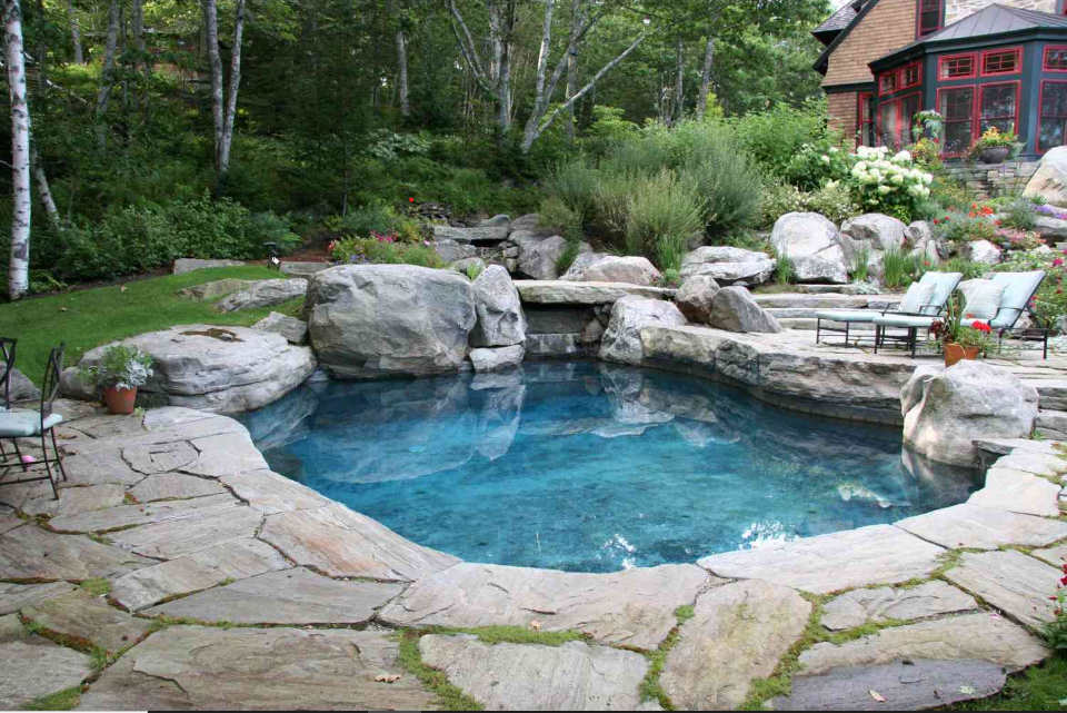 A charming backyard pool framed by rugged rocks and a sturdy rock wall, offering a peaceful retreat for relaxation.